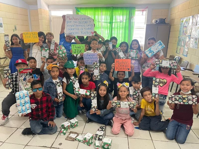 A classroom of children holding gifts and handmade signs that thank JBK Tax.